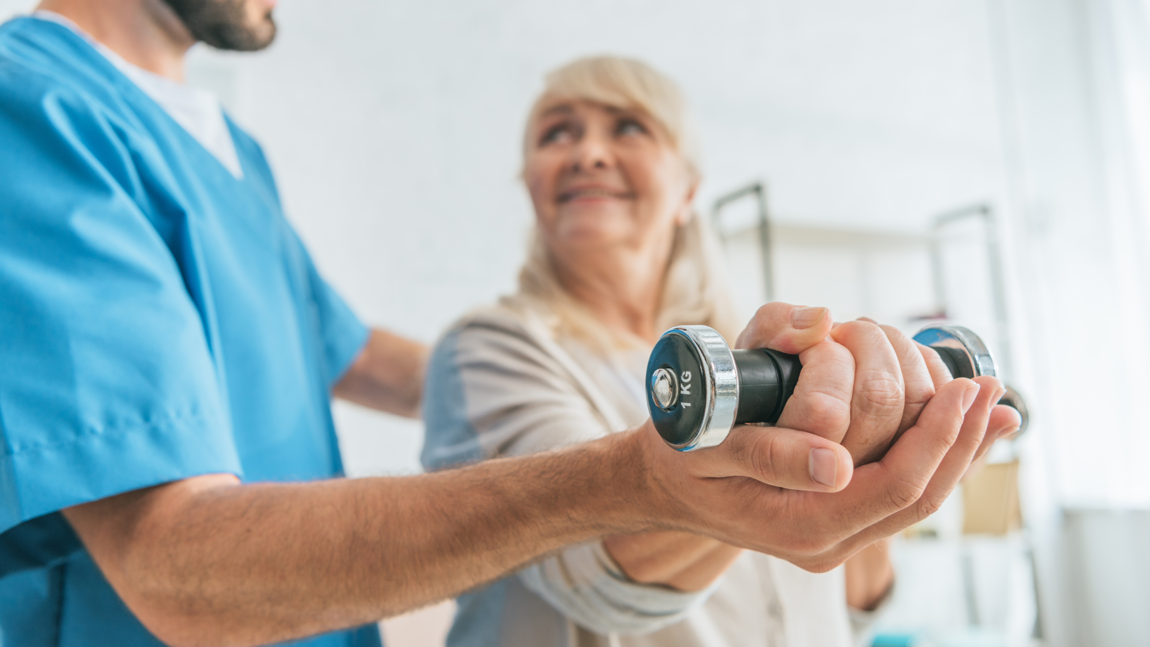 Neutral_Osteoporose_Nahaufnahme einer Sozialarbeiterin, die einer lächelnden Seniorin beim Trainieren mit Hanteln hilft_envatoelements