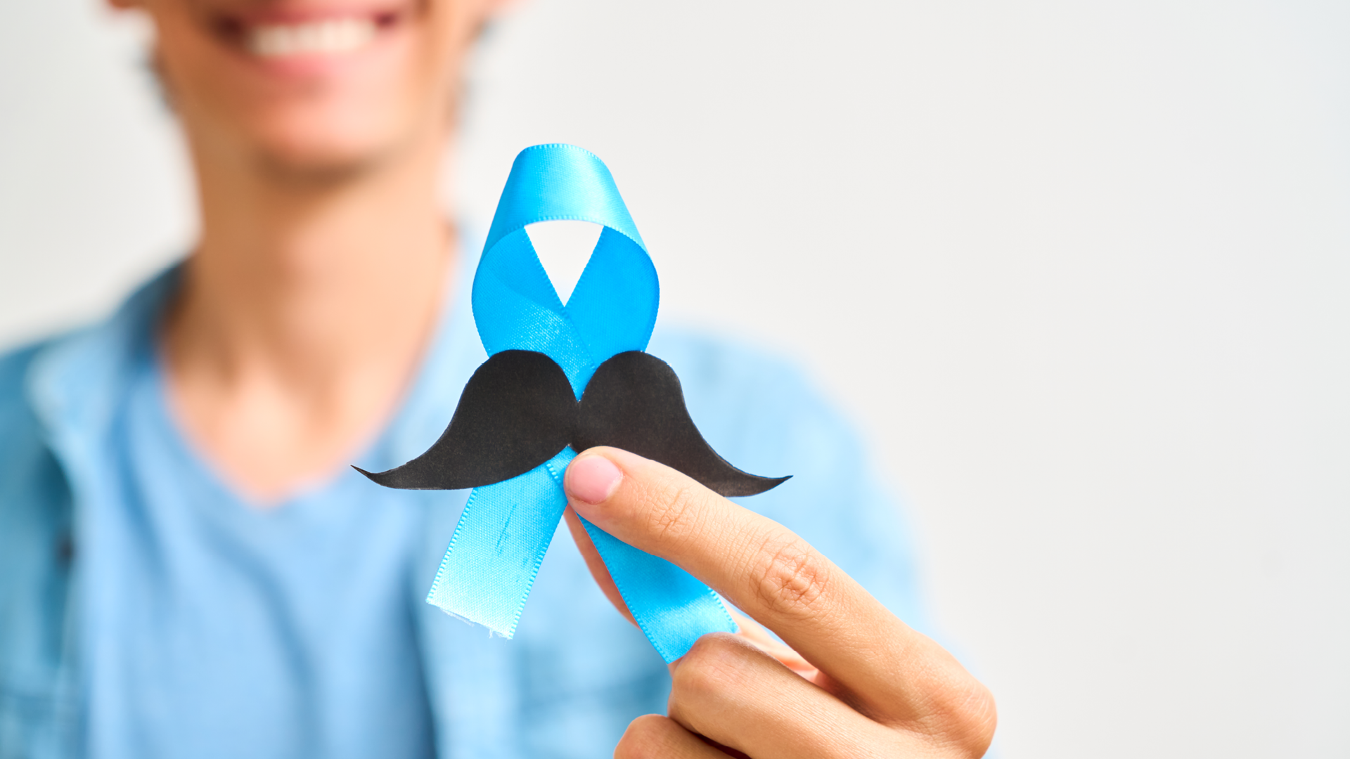 Neutral_Movember_Cheerful Latin man showing blue ribbon with mustache. Prostate cancer, awareness concept, men Health_envatoelements Movember Männergesundheit